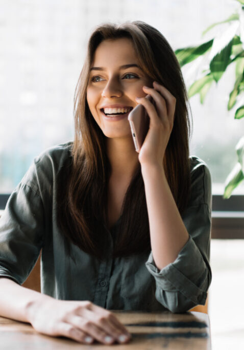 Young beautiful woman using mobile phone in modern coffee shop. Cute smiling businesswoman holding smartphone, sitting at working place.